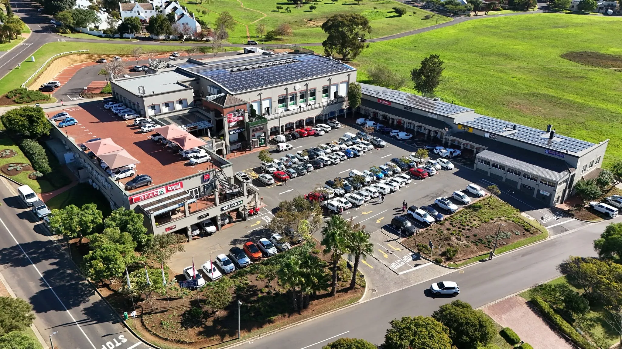 Drone view of Ipic Shopping Centre Aurora: the solar-roofed centre, its parking courts and the green fields around it.