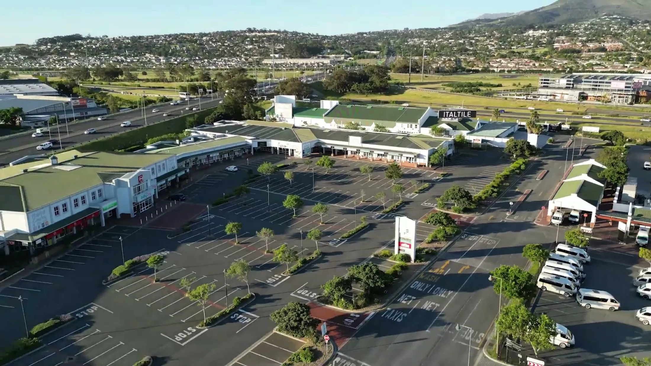 Aerial view of Habitat Centre @ the mall beside the N2 in Somerset West: the green-roofed shopfronts, parking and Helderberg behind.